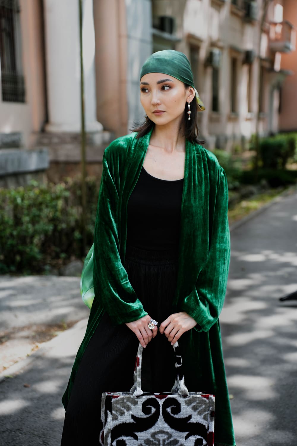 Woman in an emerald velvet TURANAI chapan and green turban holding an ikat bag on a Bishkek street